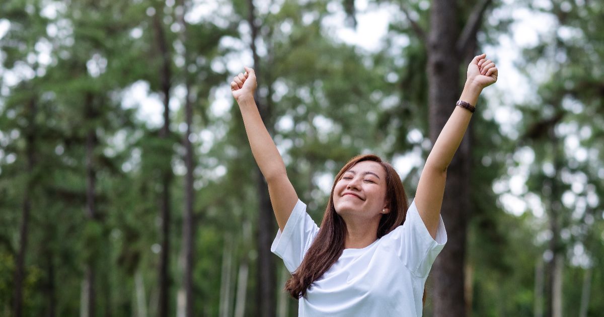 Happy woman standing in nature with arms raised feeling energized after receiving a Myers Cocktail IV infusion at Hydrate Medical in Charlotte North Carolina
